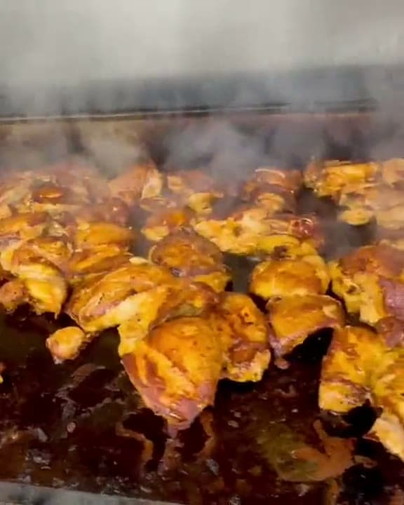 Marinated chicken sizzling and steaming on a flat-top grill