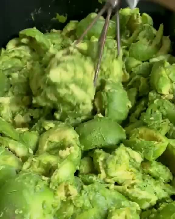 Gloved hands mashing fresh avocados into guacamole