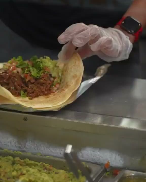 A cook folding a loaded burrito at the line