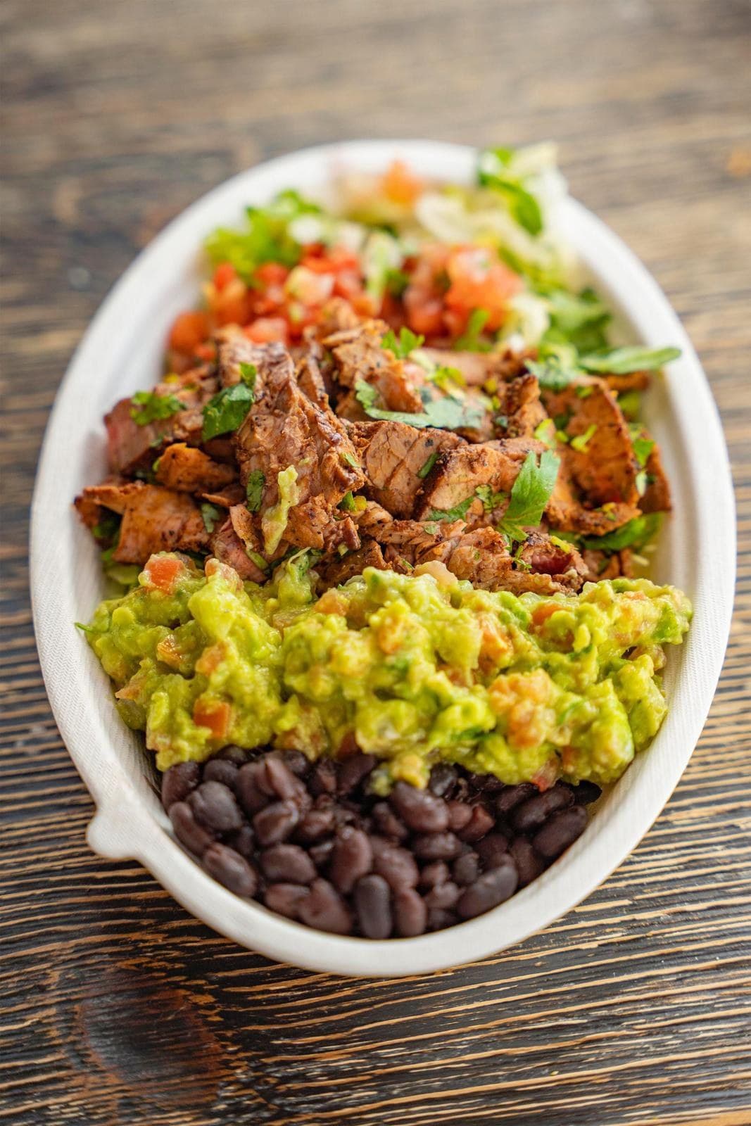 A carne asada bowl with guacamole, black beans, pico de gallo and lettuce