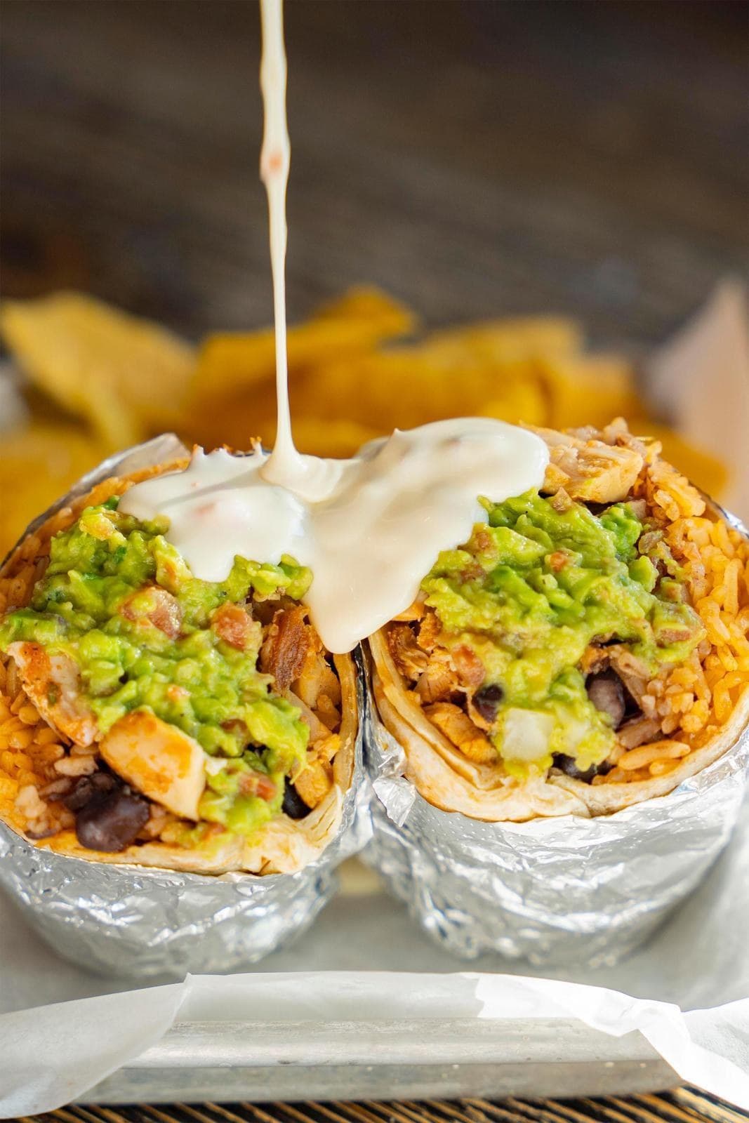 A burrito cut in half, filled with rice, chicken, black beans and guacamole, with warm queso poured on top
