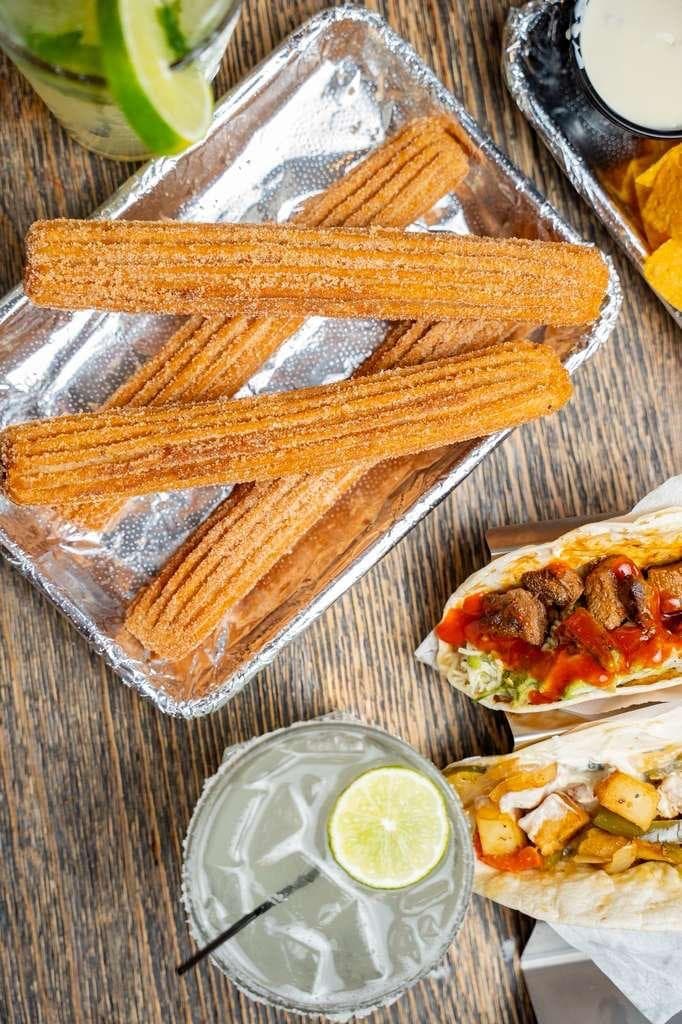 Cinnamon-sugar churros on a foil tray next to a burrito and a lime drink